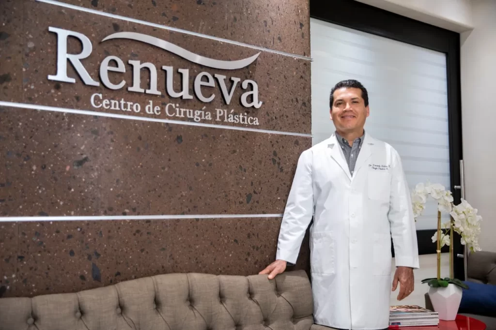 A man in a white coat standing in front of a sign for plastic surgery.
