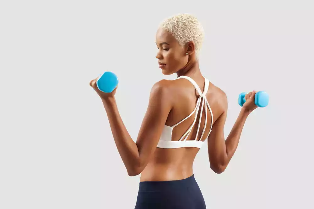 A woman wearing a sports bra with two dumbbells.
