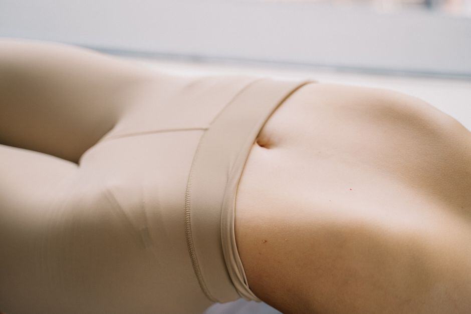 Close-up of a person lying down, wearing beige fitted clothing, with focus on the midsection and navel area.
