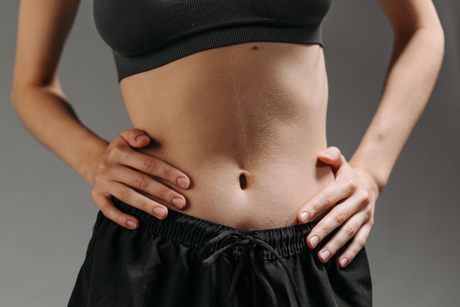 Person in athletic wear with hands on hips, showing a close-up of their bare midsection and visible line on the abdomen against a neutral background.